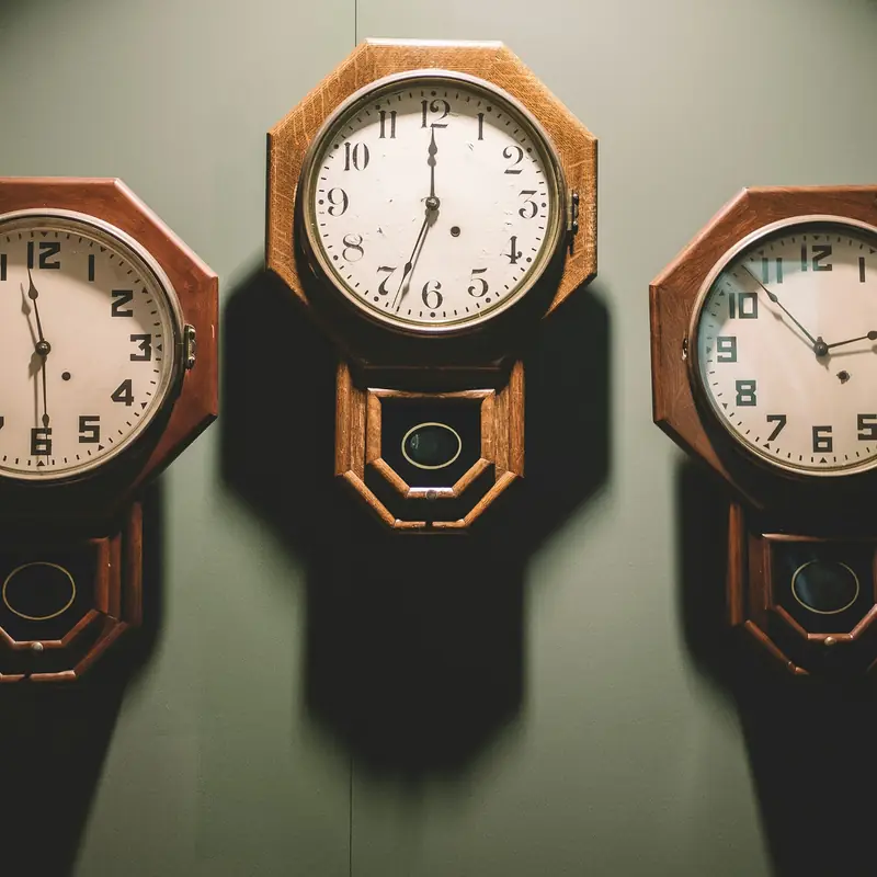 Three wooden pendulum wall clocks showing different times, side by side on a dark green wall