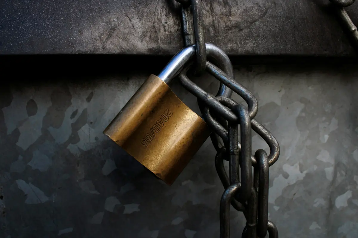 A worn brass padlock hanging from a heavy dark chain against scratched grey metal