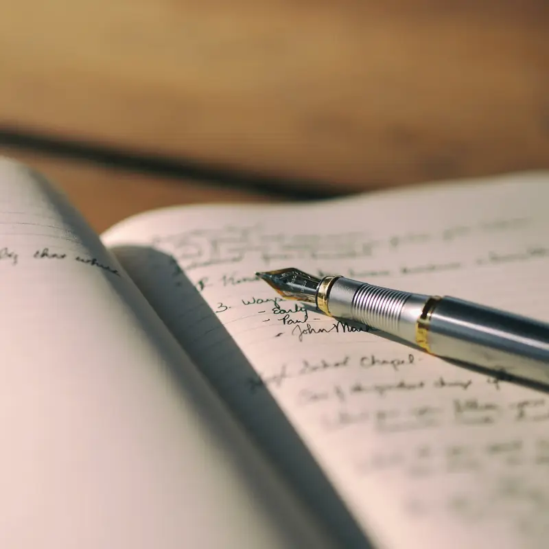 An open journal with lines of handwriting and a silver-and-gold fountain pen resting on the page, in warm light