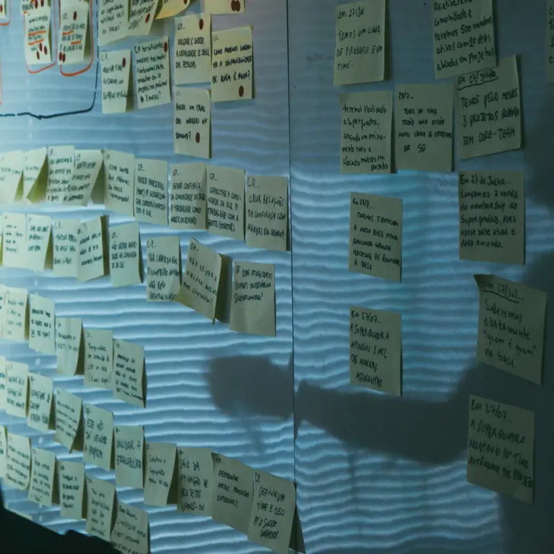 A wall covered in rows of handwritten pale yellow sticky notes in low blue light, with a person's shadow across them