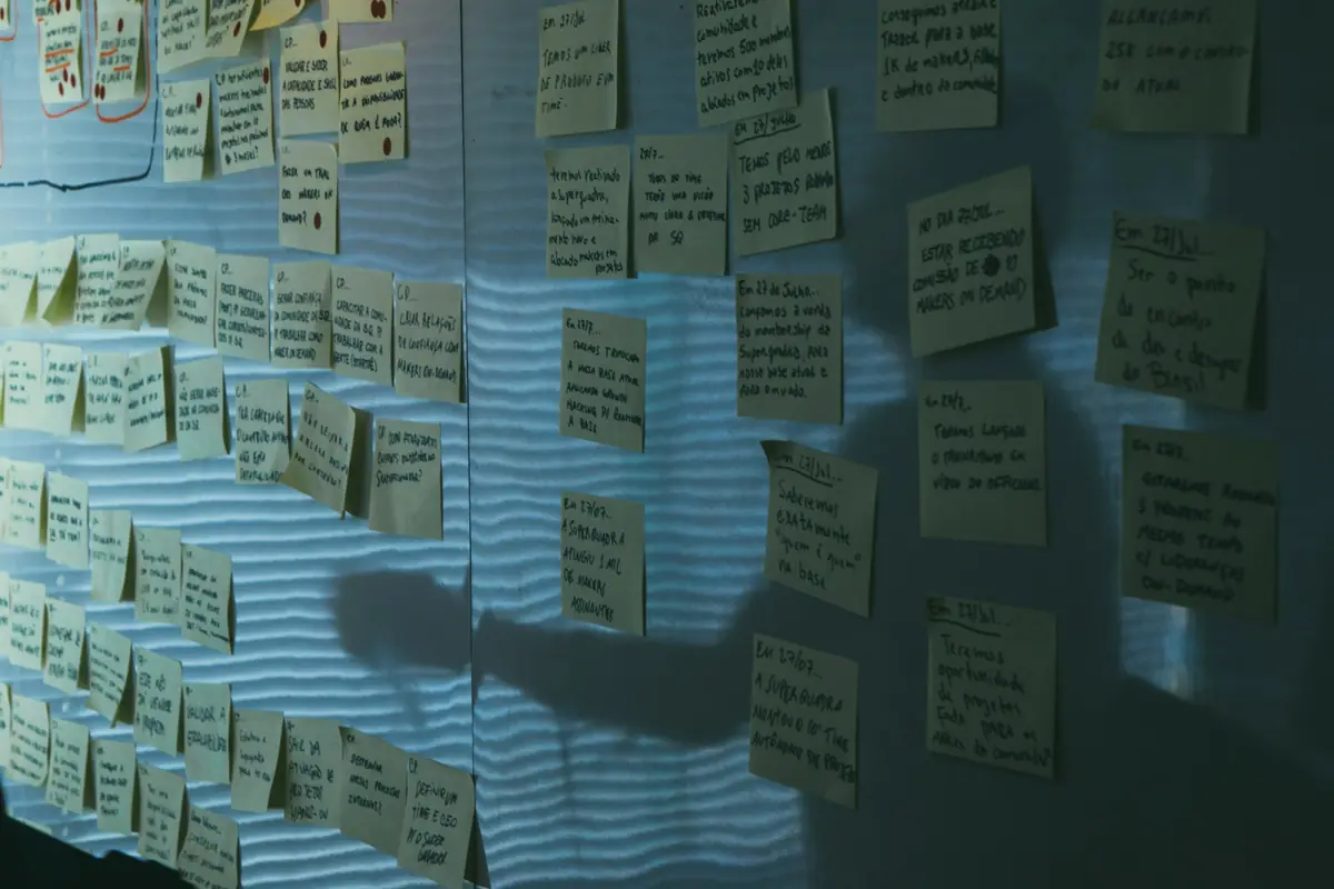 A wall covered in rows of handwritten pale yellow sticky notes in low blue light, with a person's shadow across them